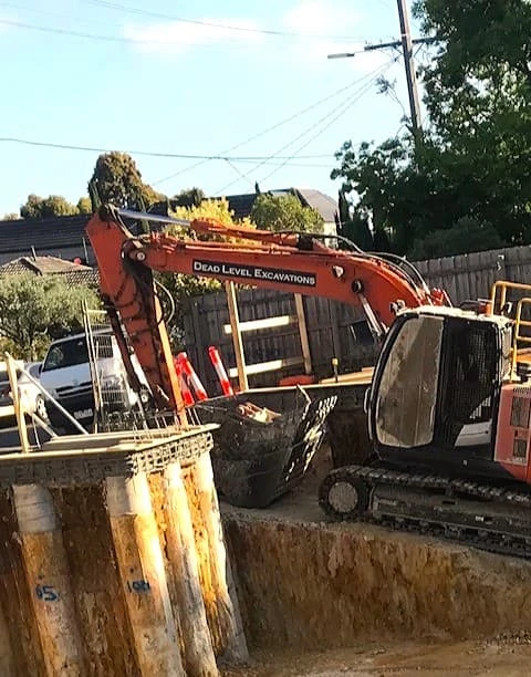 Excavator moving up a ramp from a basement site cut with bored piers.